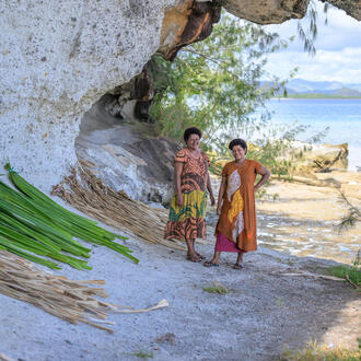 Two women pose on beach next to leaves laid out for drying